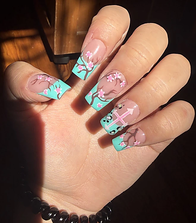 Uñas acrílicas largas con puntas turquesa y flores rosas pintadas, con luz de atardecer