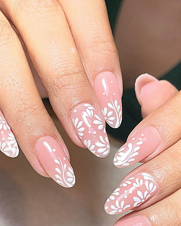 Uñas almendra largas en nude con flores blancas pintadas a mano en las puntas