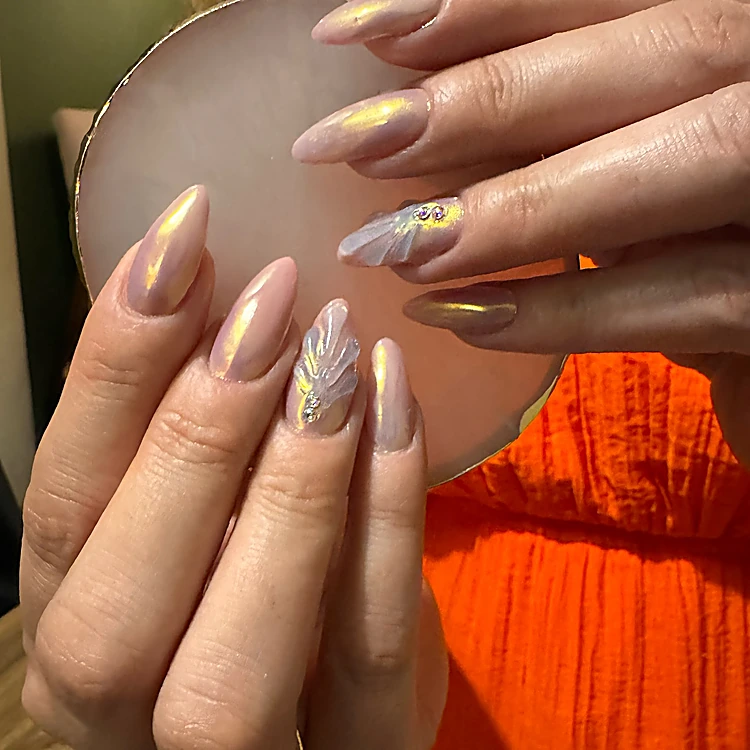 Uñas almendra largas en nude con efecto perlado y dos uñas con concha en relieve y strass