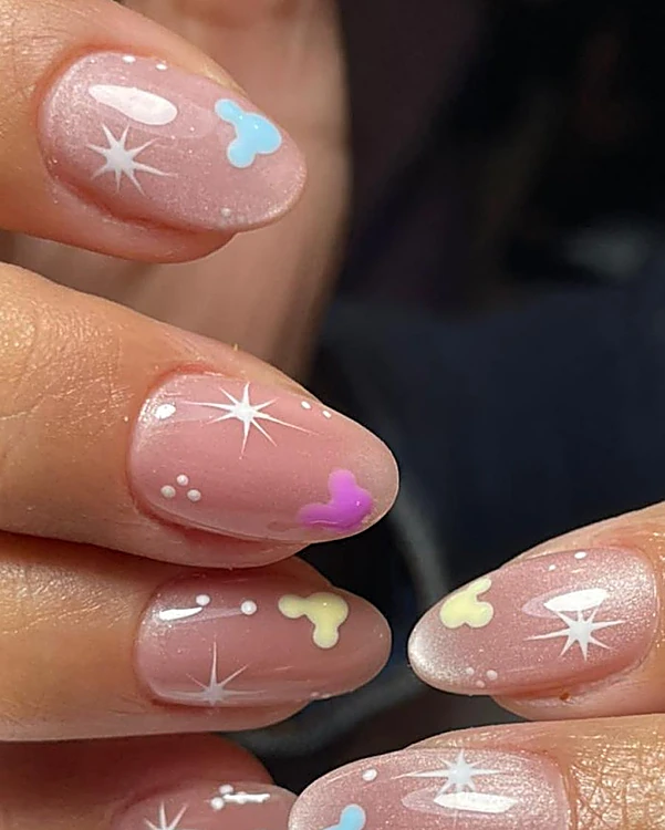 Uñas almendra nude con corazones pastel azul, lila y amarillo y destellos blancos
